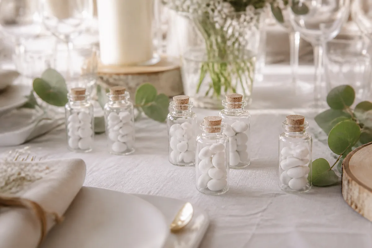 Petites fioles en verre remplies de dragées blanches et posées sur une nappe claire
